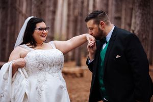 A bride and groom share a joyful moment in a rustic outdoor setting surrounded by tall trees.