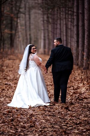 A wedding couple walks through a forest covered in fallen autumn leaves in a series of romantic poses.