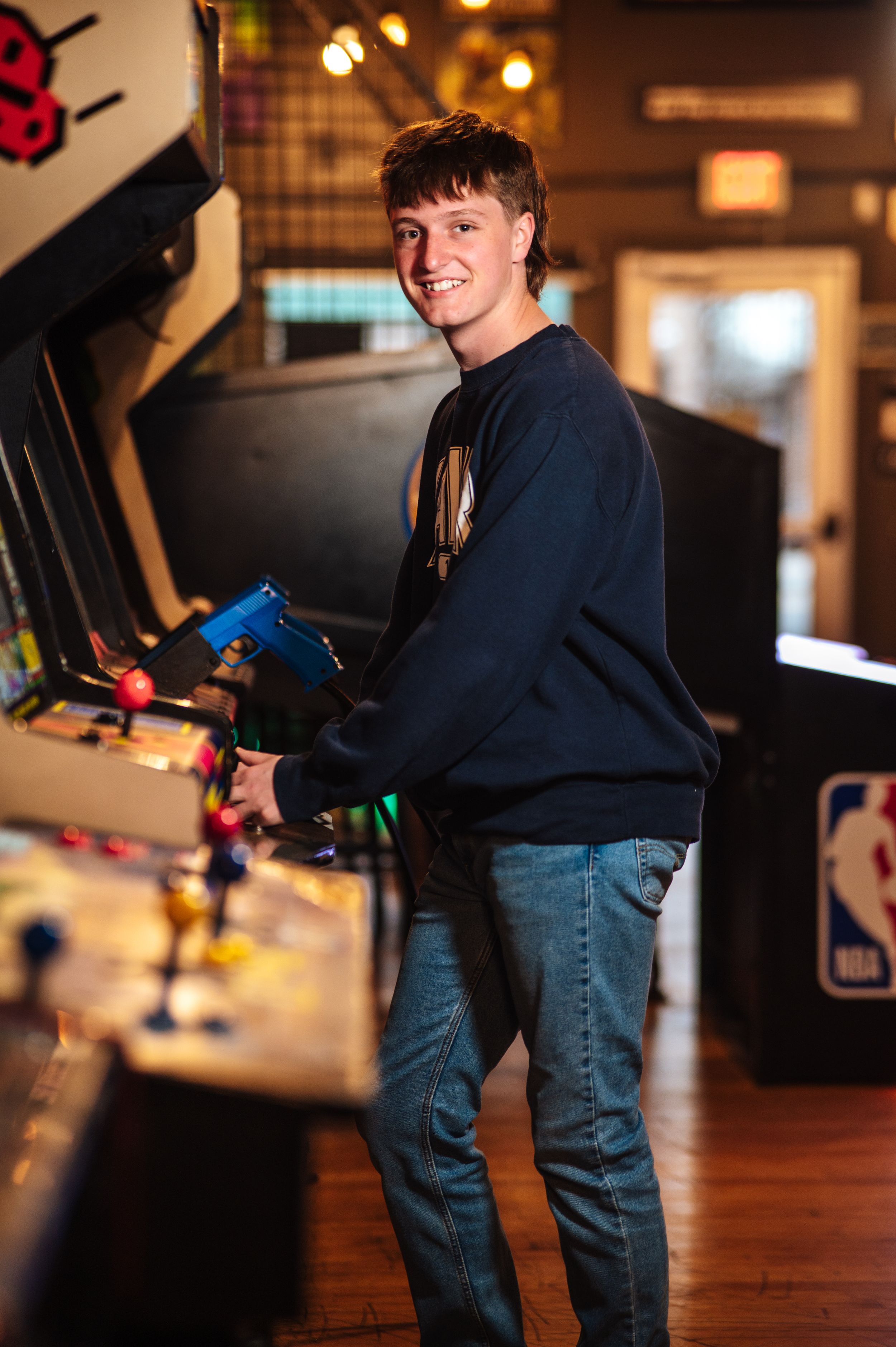 Someone in a navy sweater and jeans plays an arcade game in a dimly lit entertainment venue In Findlay, Ohio.