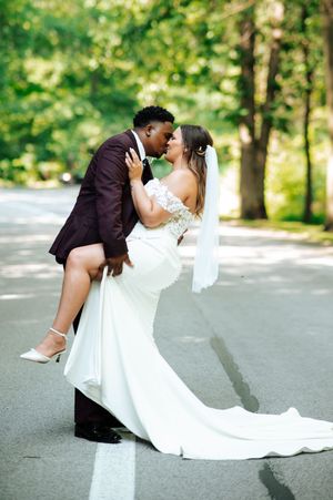 A romantic wedding couple shares a kiss in a lush green outdoor setting on a paved path.