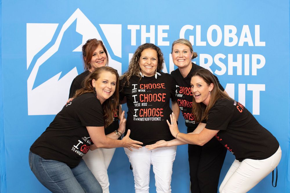A group in black t-shirts poses playfully together at a global leadership summit event.