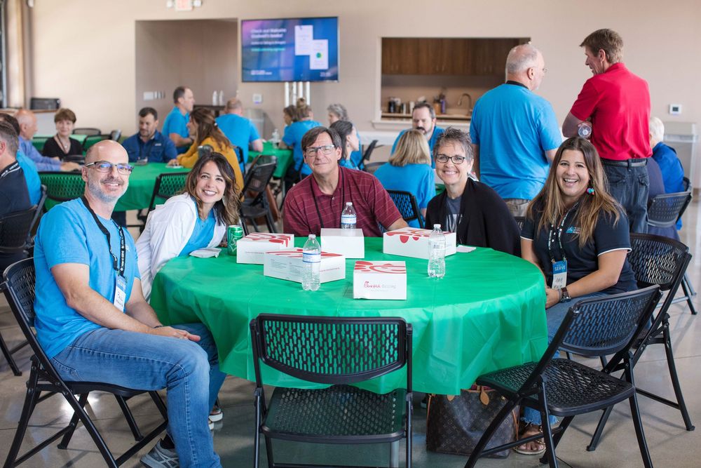A group of attendees sits around a round table with a green tablecloth at a conference or meeting event.