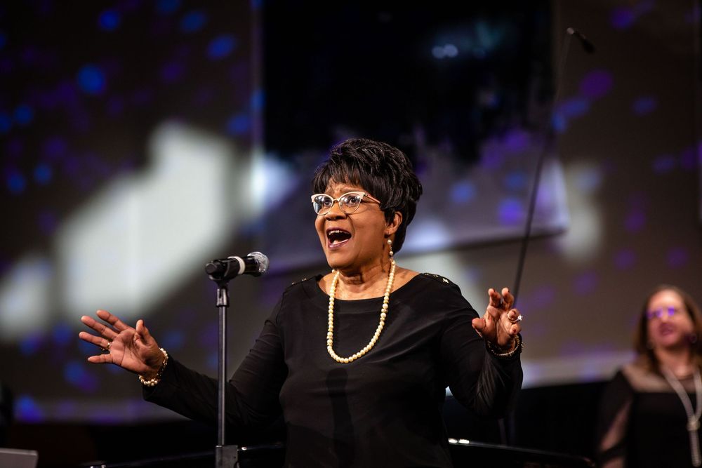 A performer sings passionately on stage during a concert with dramatic lighting and a microphone stand.