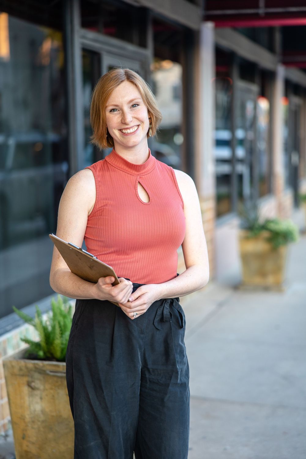 Professional headshots of a person in a coral sleeveless top and black pants standing in front of a modern building exterior.