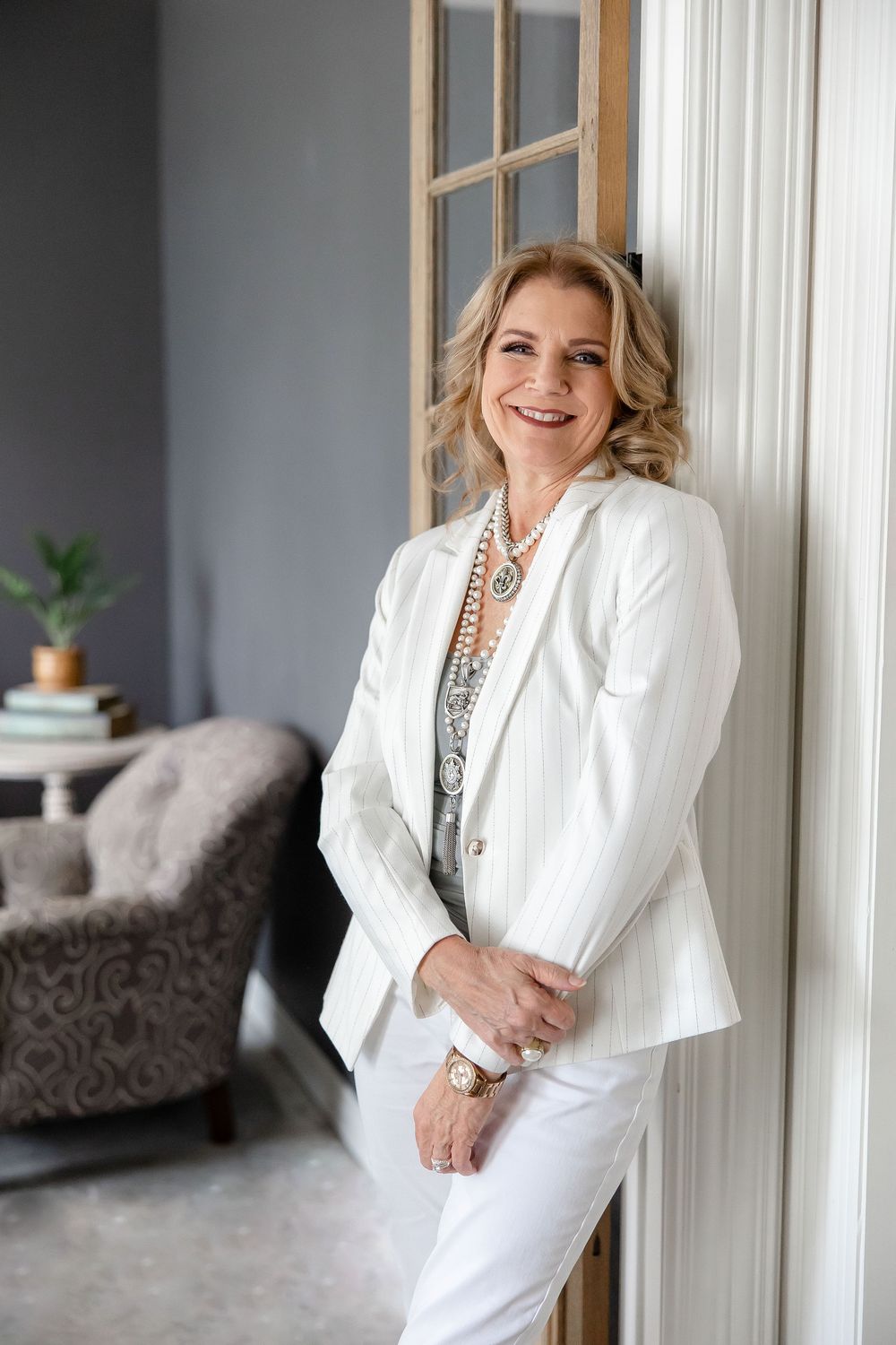 Professional headshots of woman in white blazer and jewelry posing against gray wall in indoor setting.