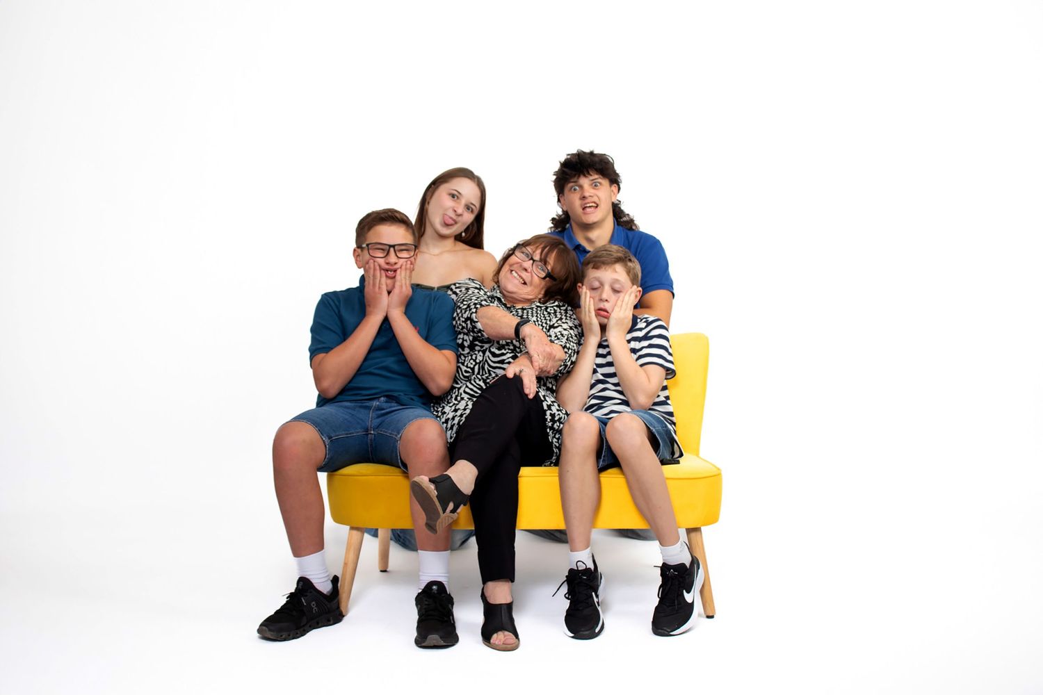 A casual group portrait of people seated on a yellow bench against a white backdrop.