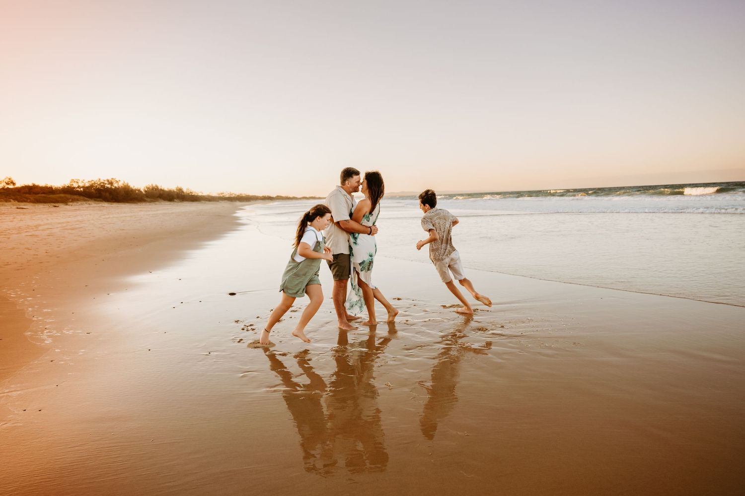 A family plays together in the ocean waves at the beach during sunset.