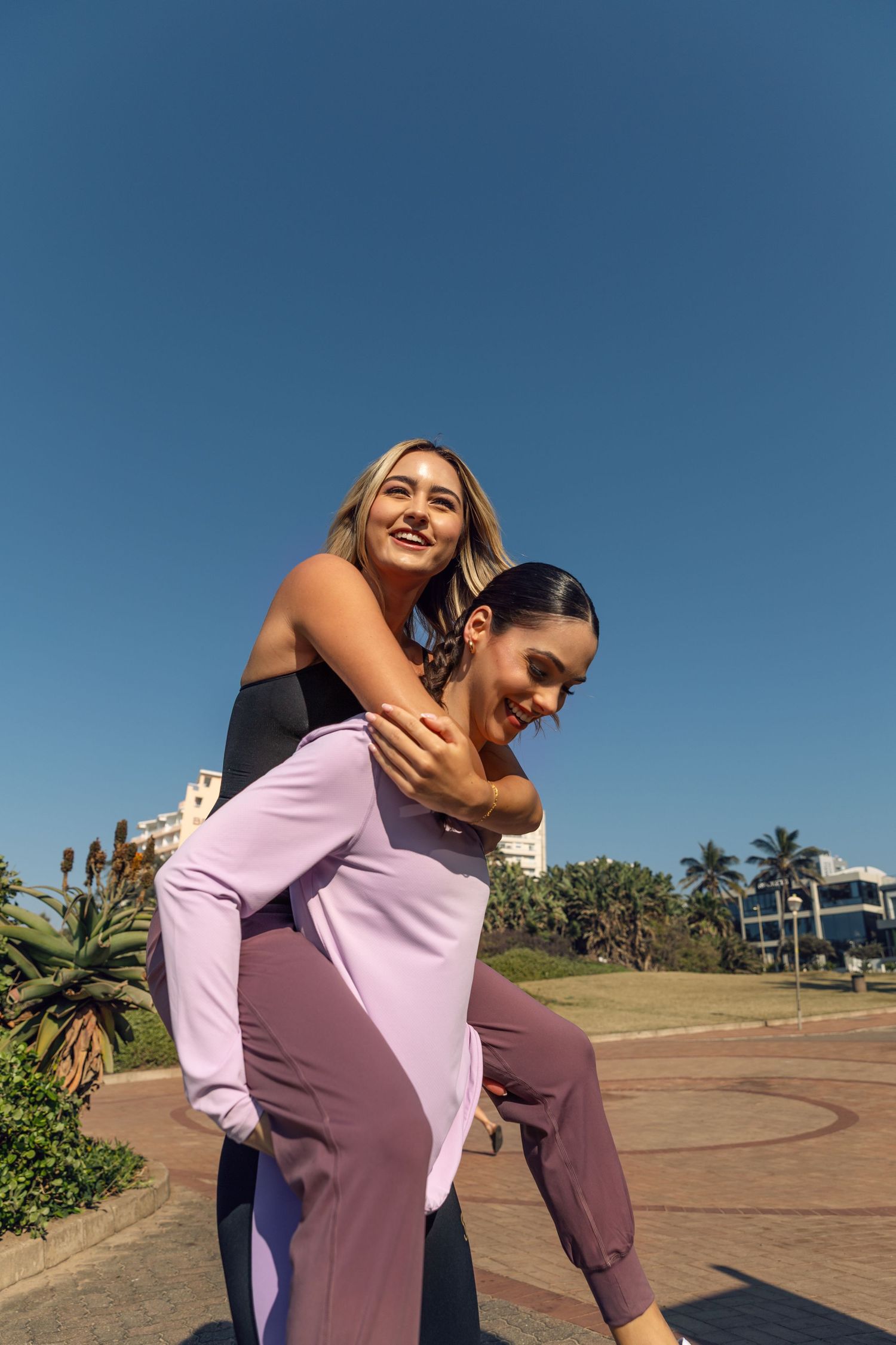 Two friends having fun outdoors with a piggyback ride against a blue sky and tropical landscape setting.