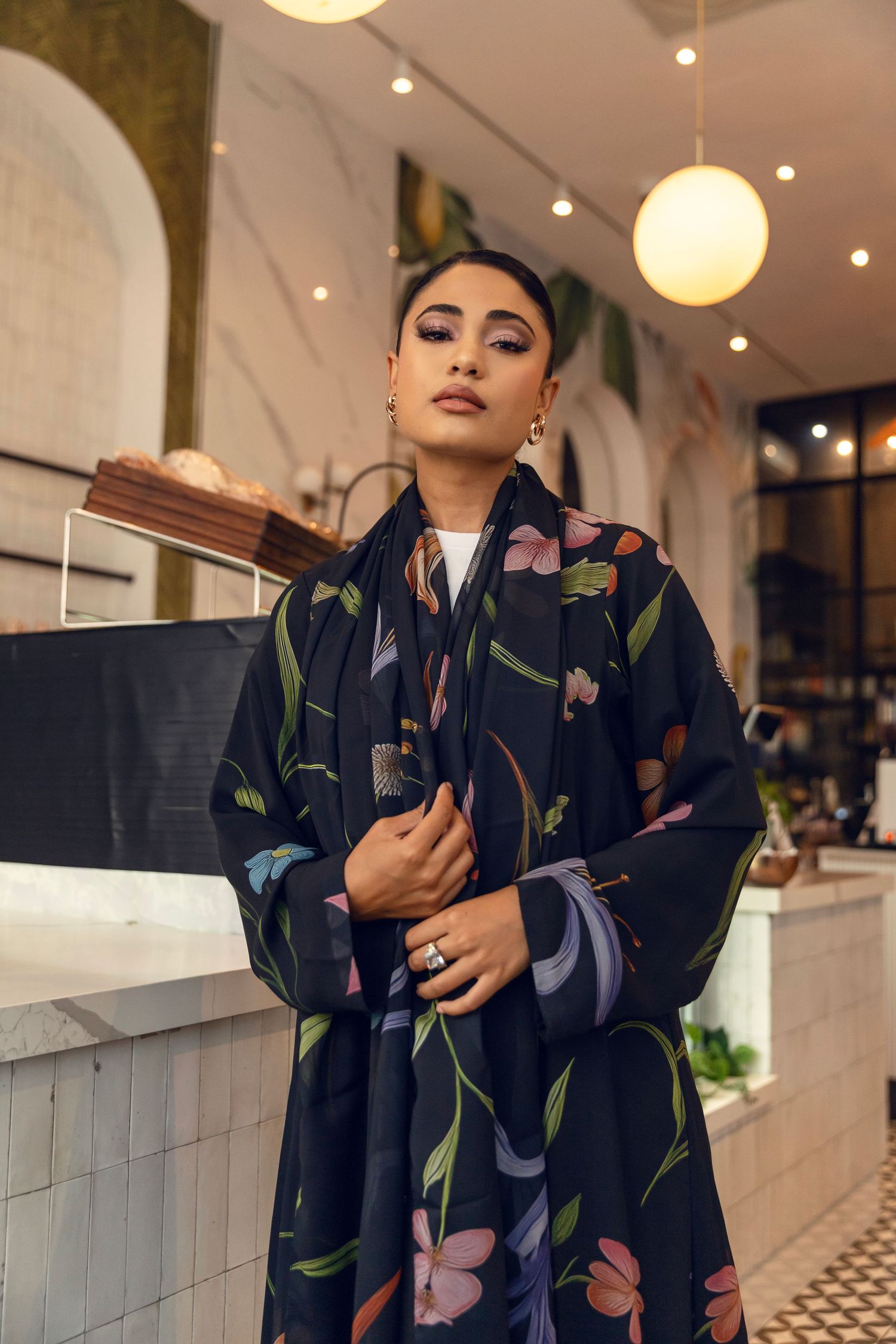 A floral patterned navy kimono-style outfit is elegantly modeled in a restaurant setting with warm lighting.