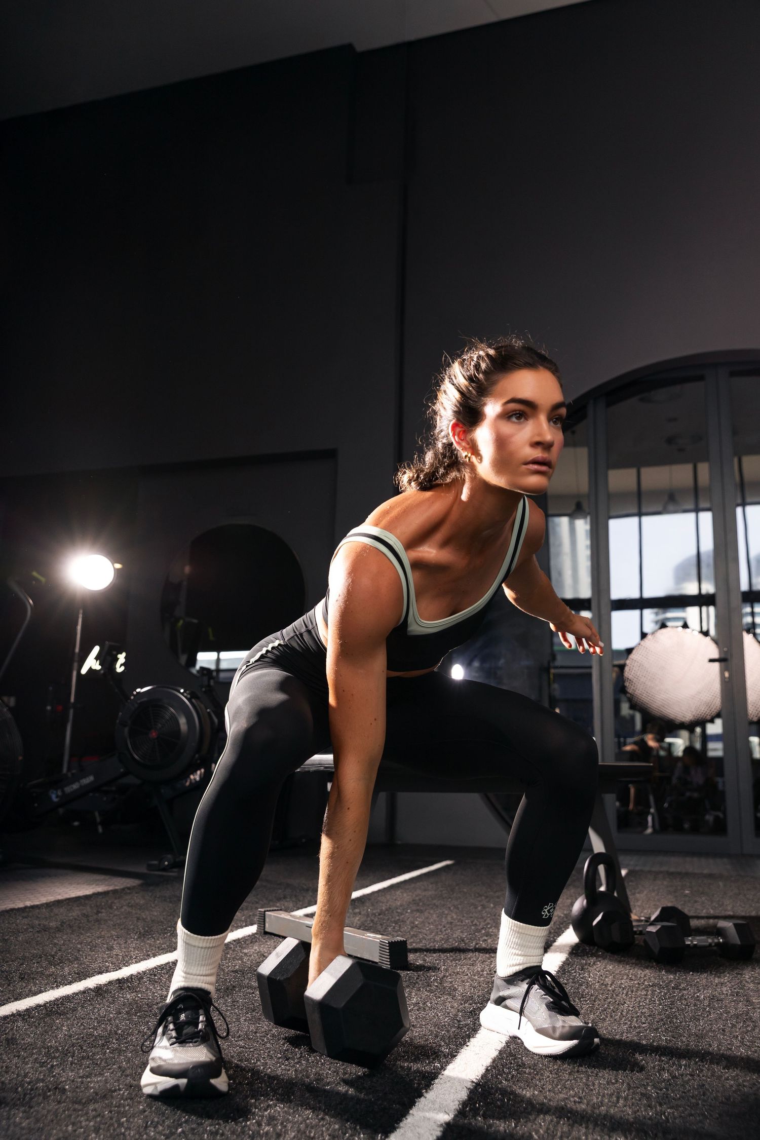 Athletic woman performing dumbbell rows in a modern gym, wearing black leggings and a sports top.