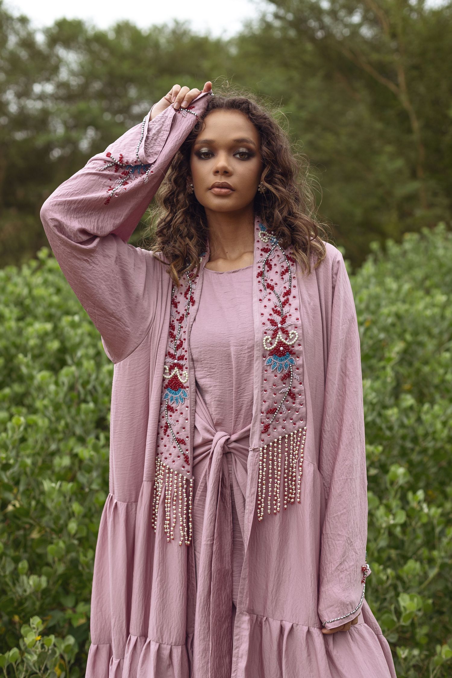 Dusty rose maxi dress with floral embellishments and fringe details photographed in a natural garden setting.