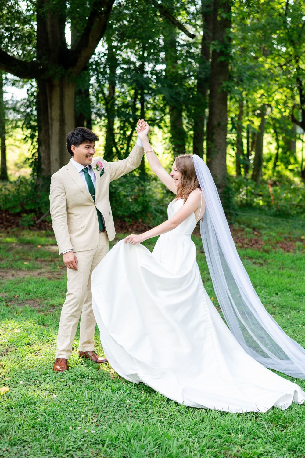 Bride twirling in her wedding dress while holding hands with the groom beneath tall trees