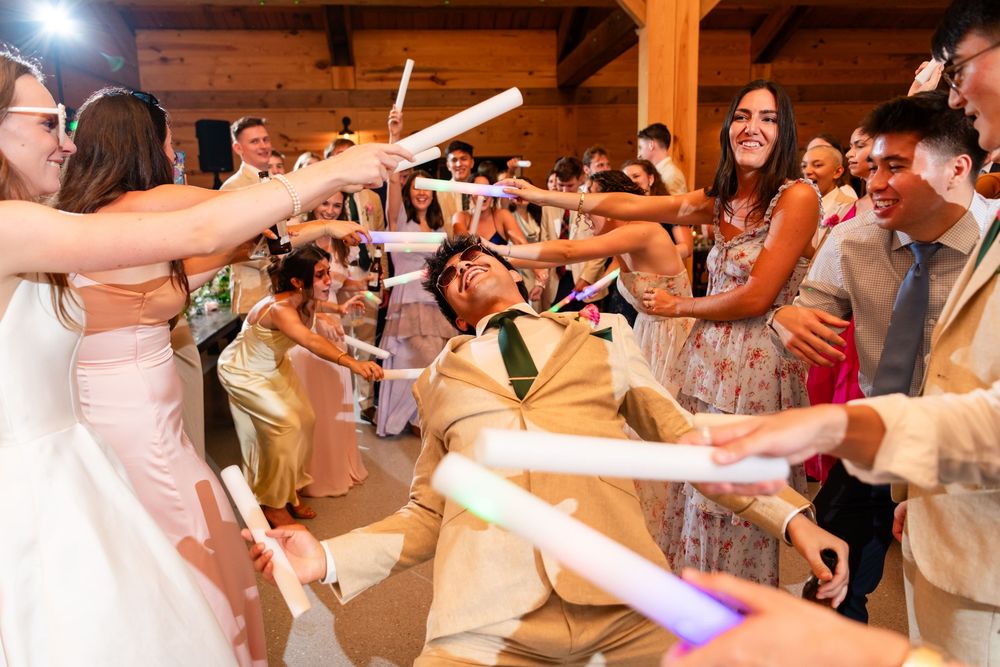 Groom doing the limbo and laughing on the dance floor as wedding guests surround him with glowing foam sticks