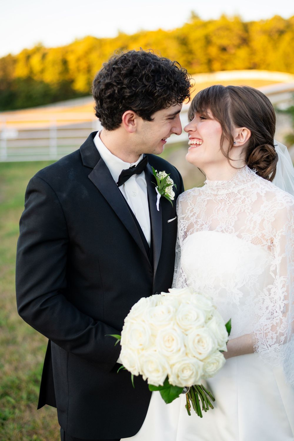 Bride and groom smiling at each other during an outdoor wedding portrait at Berlin Farms, with the bride holding a bouquet of white roses