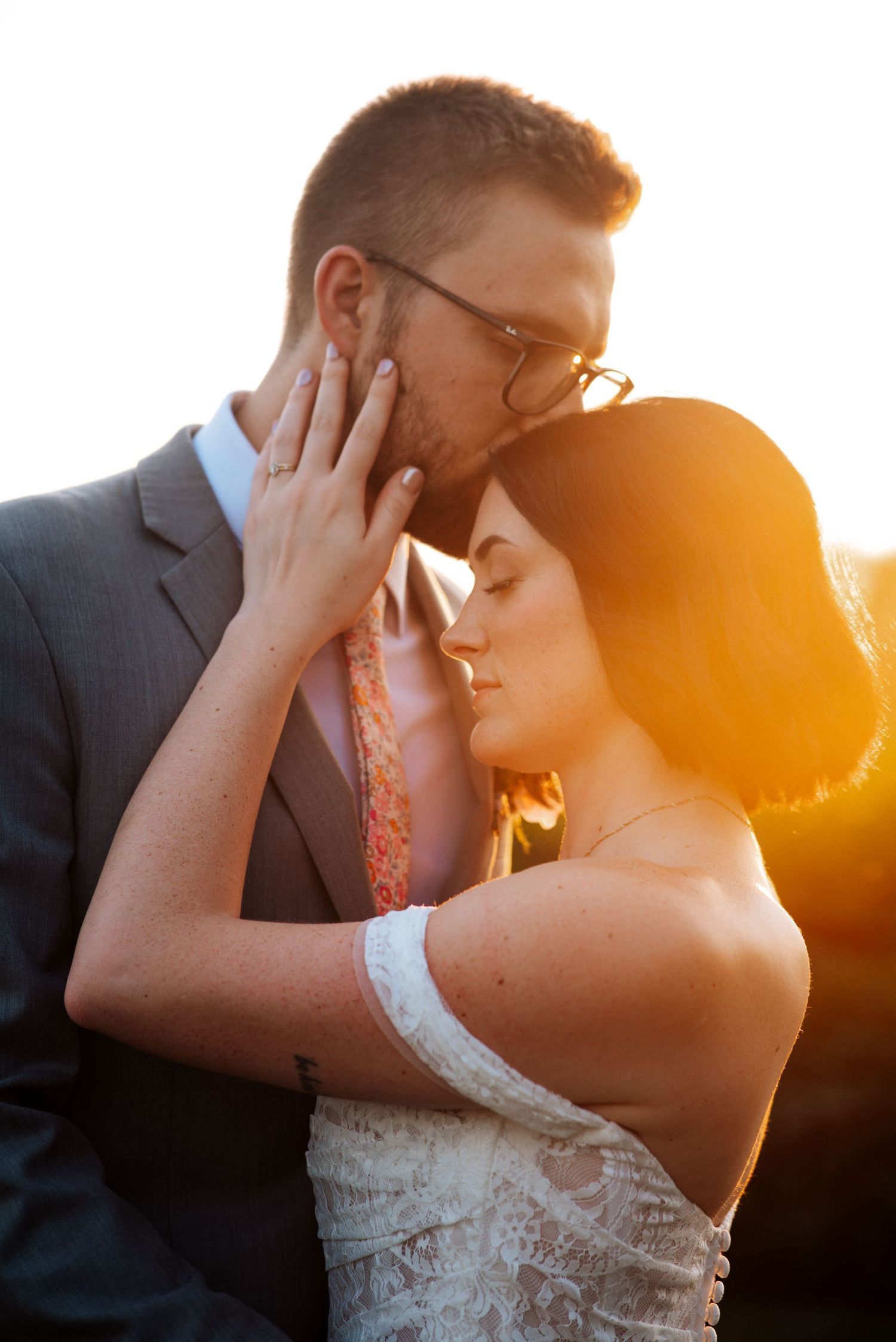 A wedding couple shares a romantic kiss during golden hour sunset with a beautiful warm glow in the background at Bloom & Bower in Risingsun
