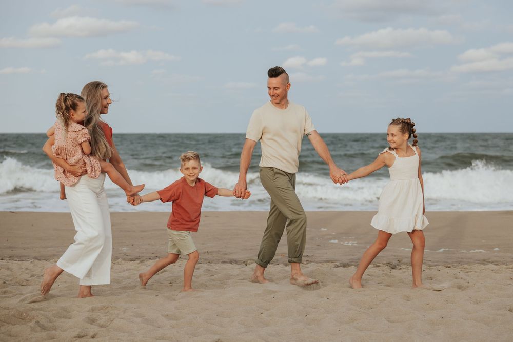 Joyful family holds hands and walks together along a sandy beach at sunset with ocean waves in background.