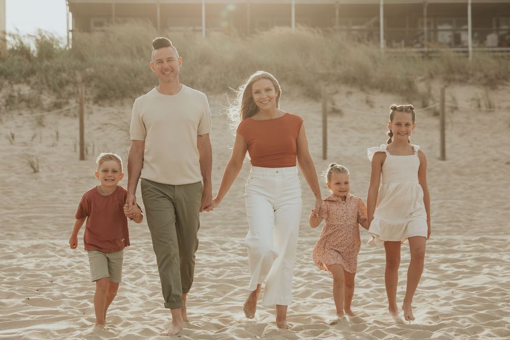 Family in coordinating outfits walking together on sandy beach during sunset.