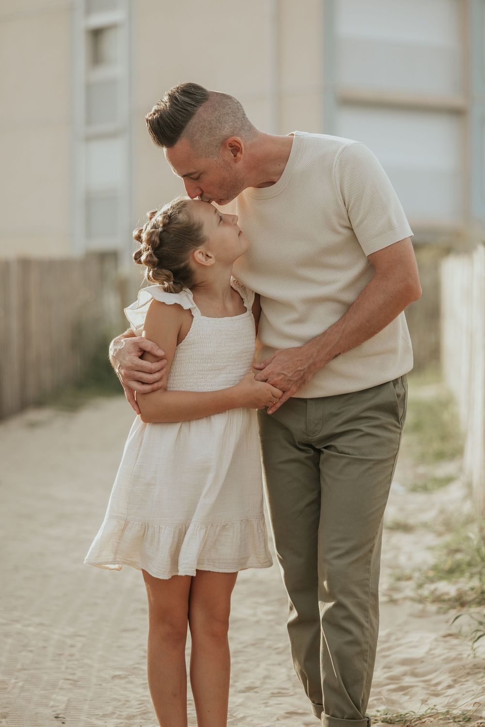 A tender moment between an adult and child in white dress sharing a kiss in outdoor lighting at sunset.