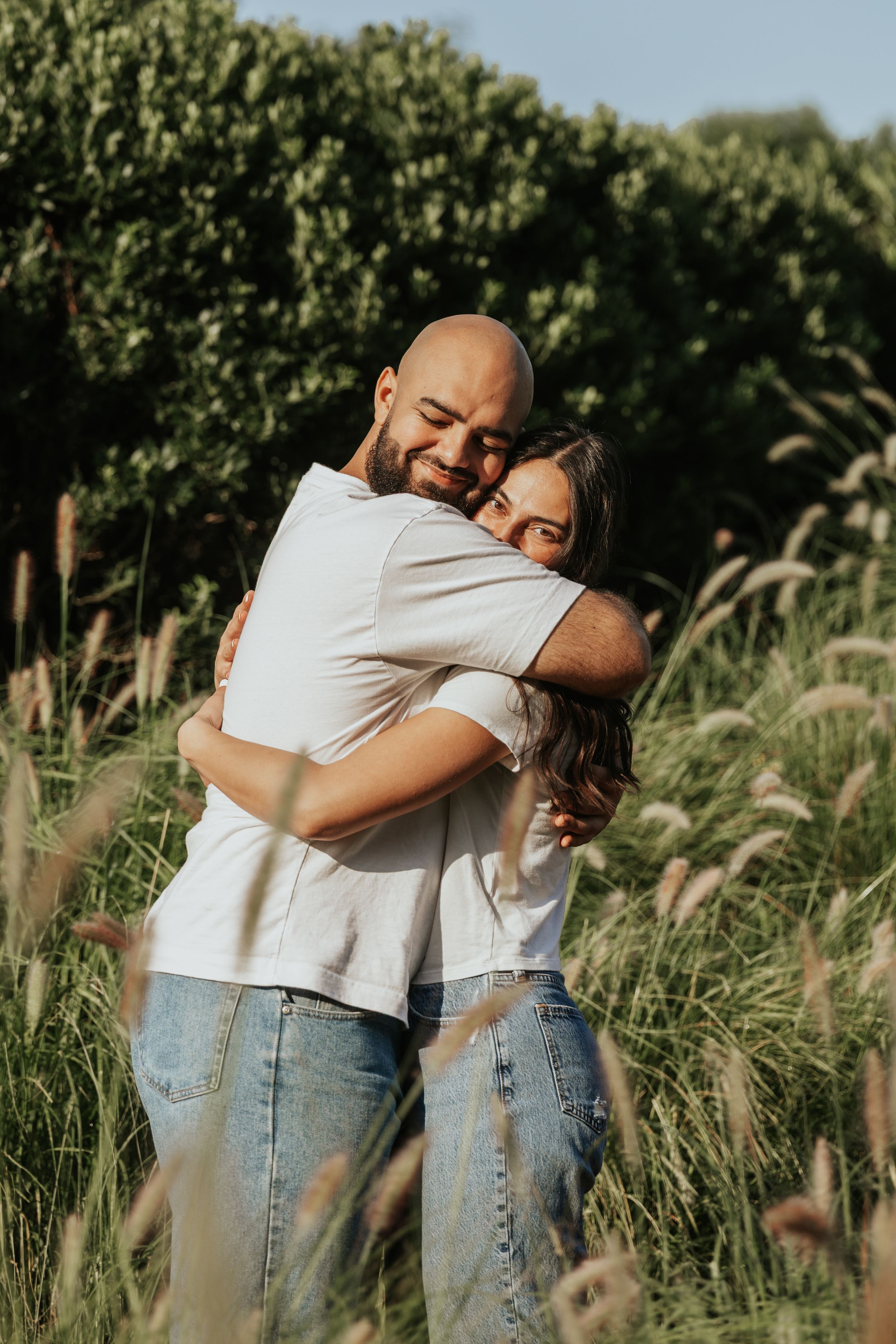 Friends share warm embraces in a scenic field with tall grass and natural sunlight.