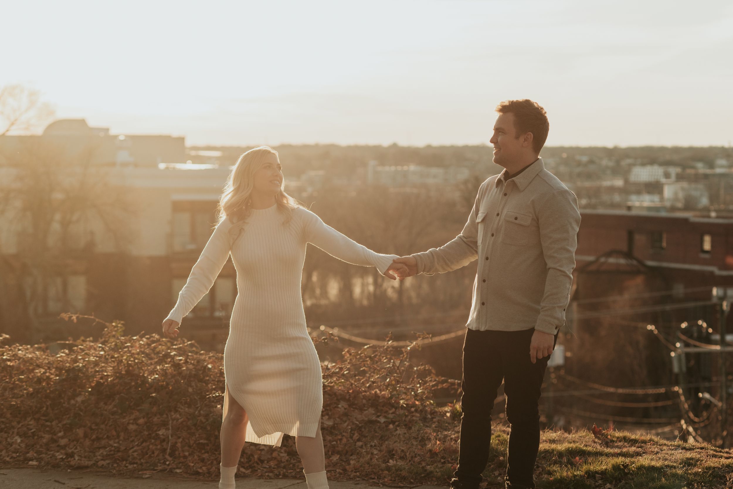 Couple dances together at sunset with city rooftops in the background.