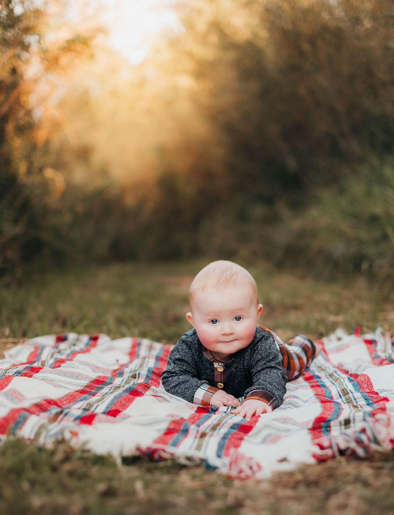 Baby in grey sweater lying on red and white blanket during golden hour sunset.