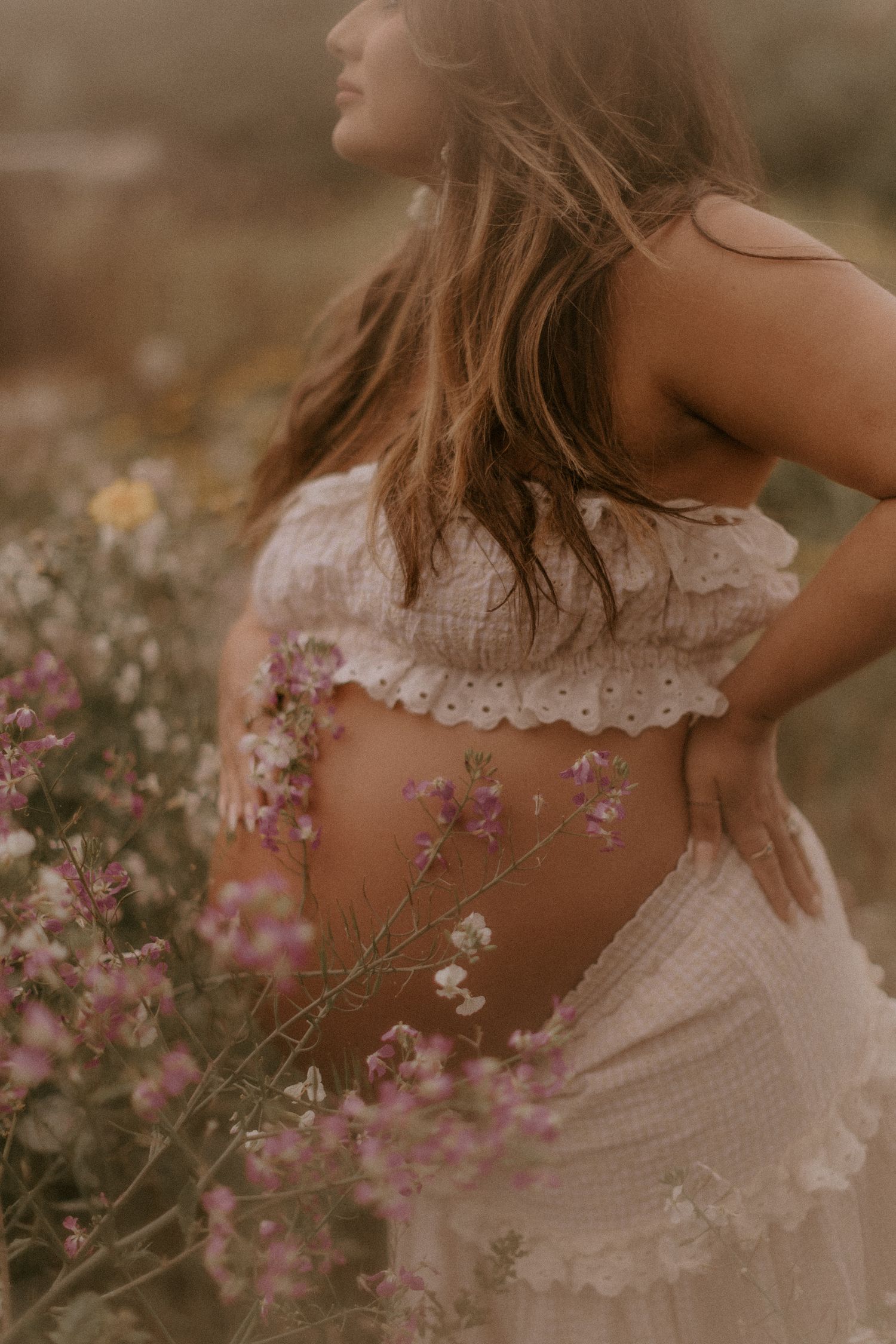 A series of romantic maternity photos showing a person in white lace dress surrounded by pink wildflowers in soft golden light.