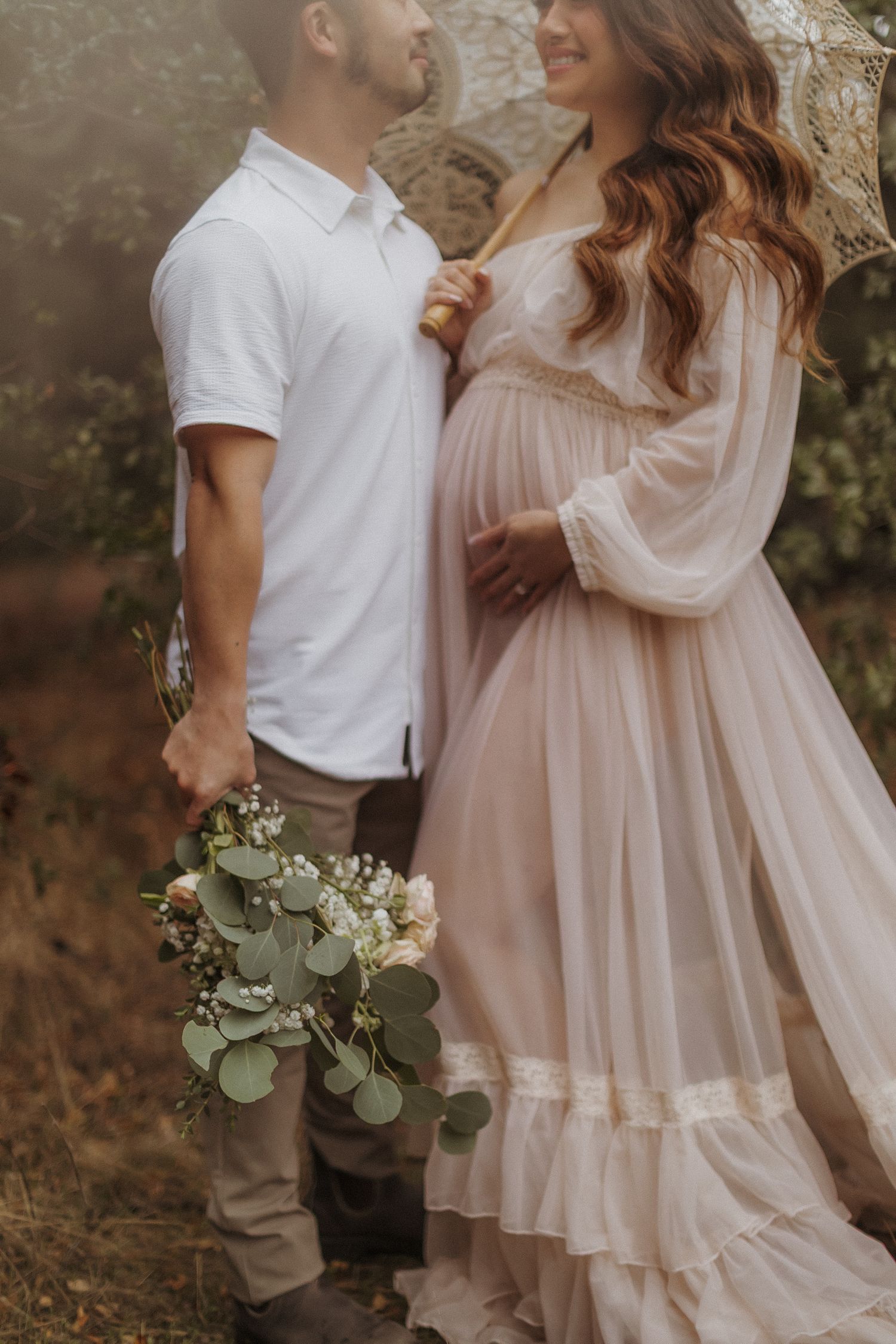 Romantic outdoor photoshoot with couple in white and cream clothing holding eucalyptus stems. San Diego Maternity Photography.