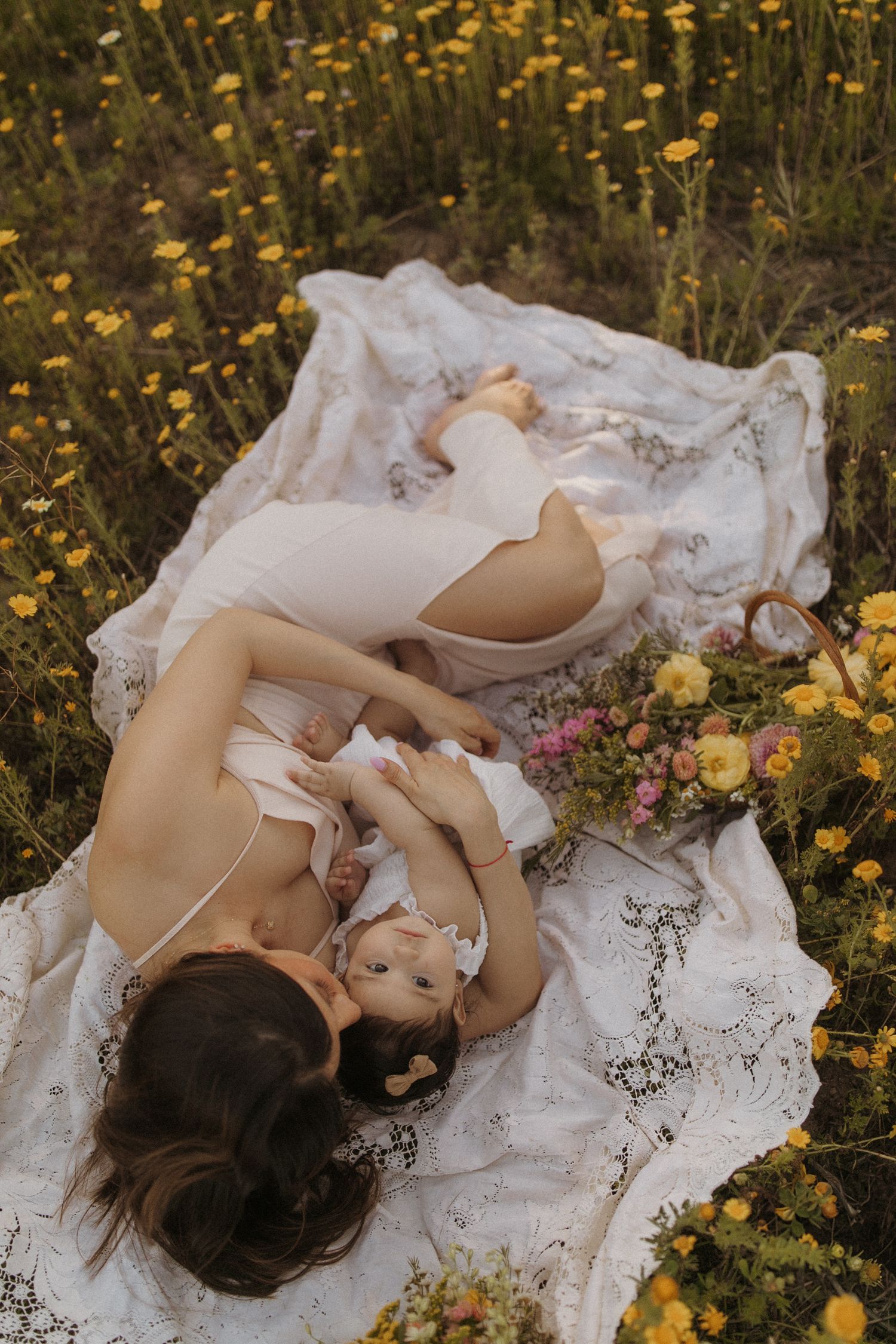 Artistic maternity photos with white lace dress among yellow wildflowers.