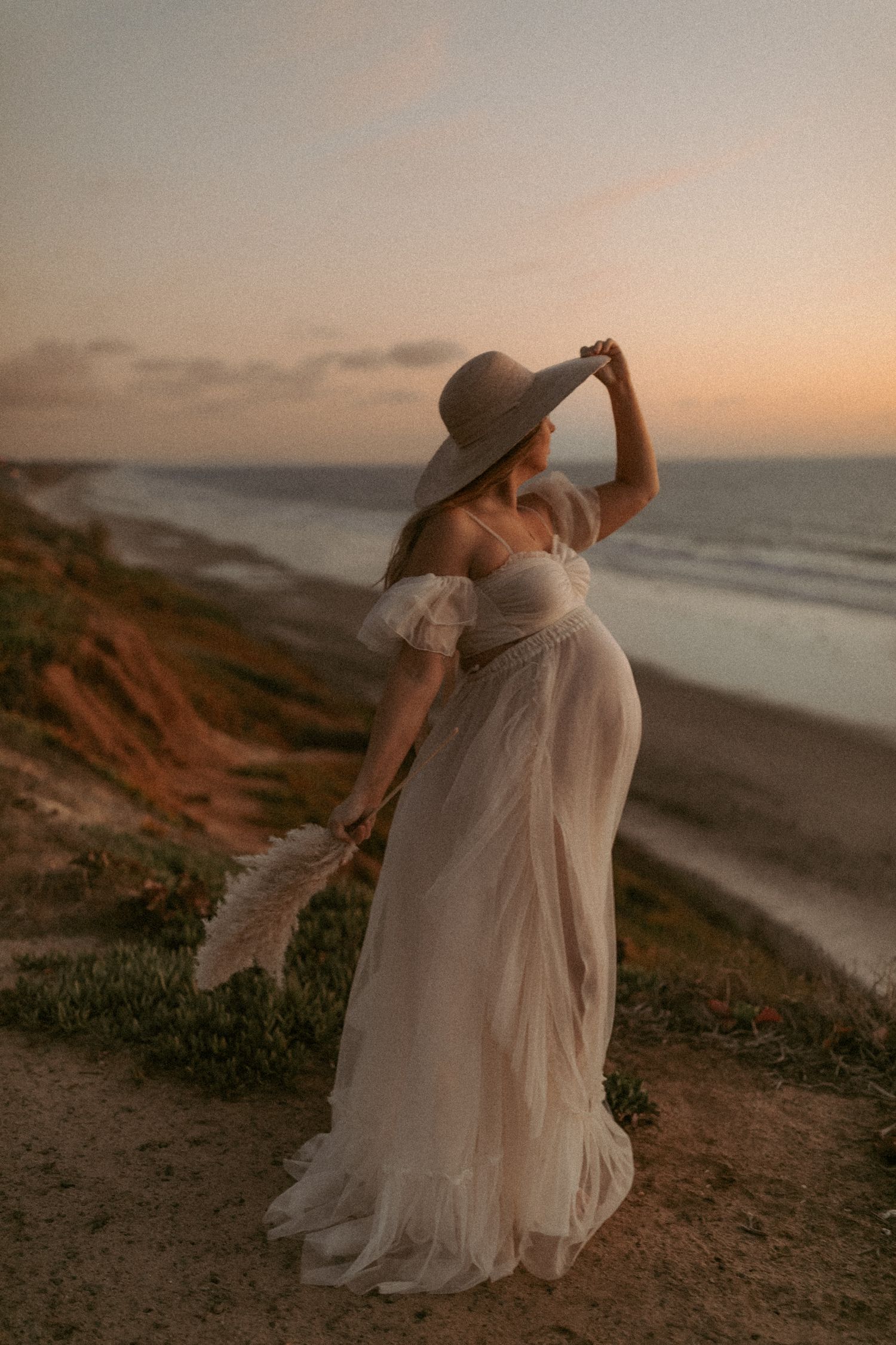 San Diego Beach Maternity Session. A moody coastal maternity session against a sunset backdrop along rugged cliffs by the ocean.