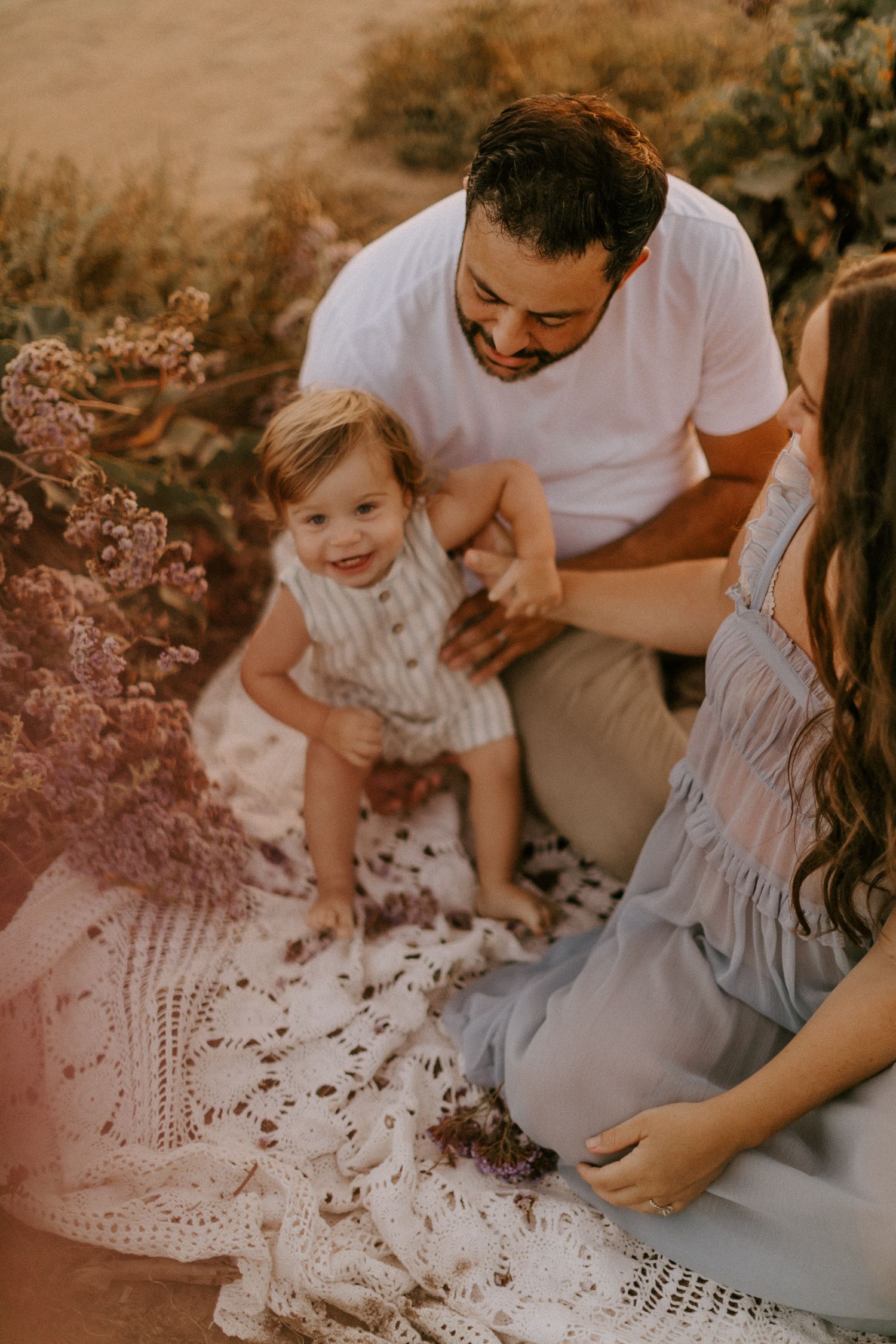 Candid outdoor San Diego maternity photo session showing family moments in soft golden sunlight with flowy dress and grass background.