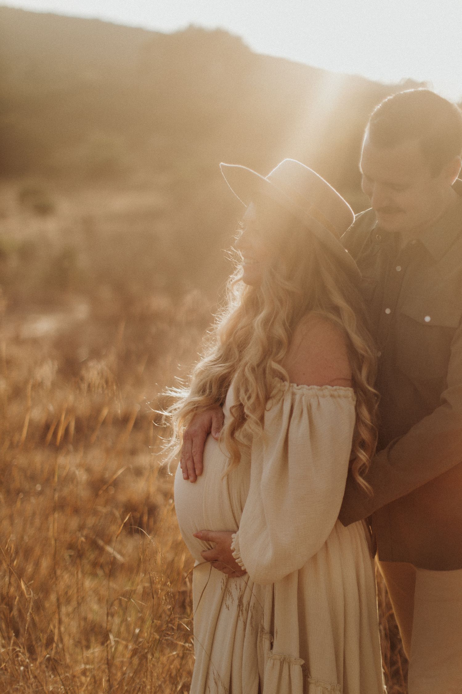 Romantic couple photos in sunlit field with flowing white dress. San Diego Maternity Photography.