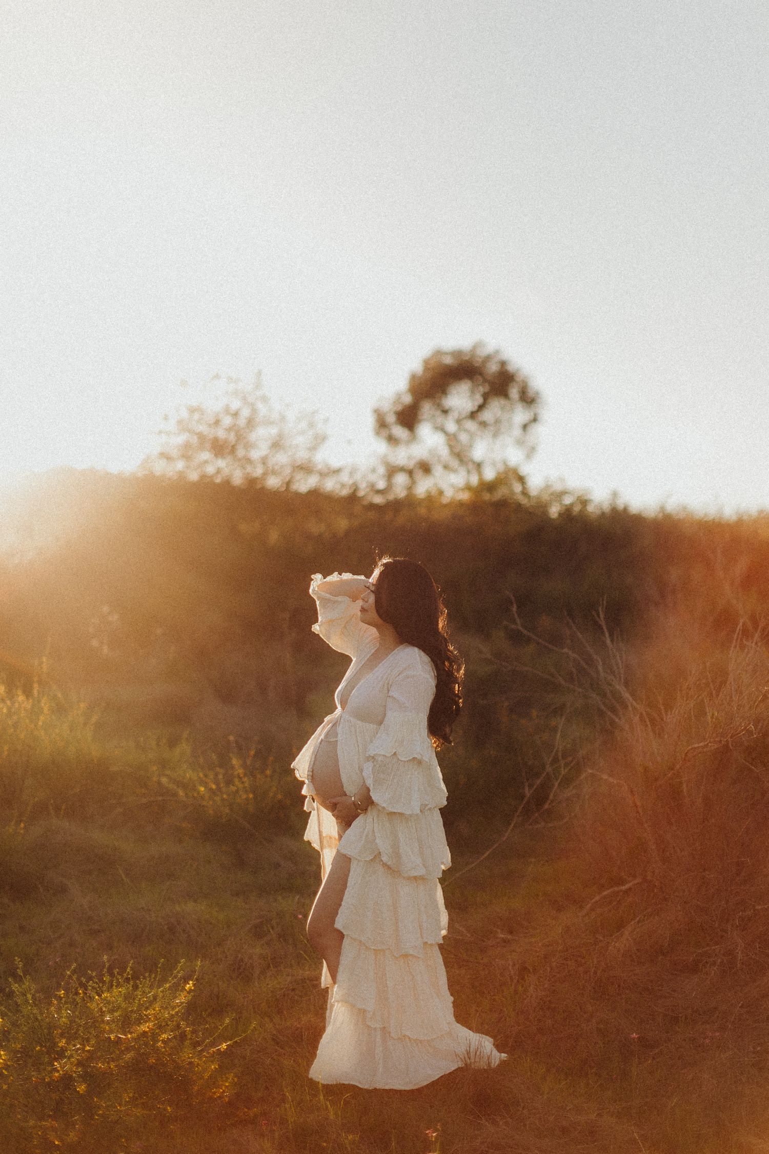 A serene maternity session in a flowing white dress gracefully in a sunlit meadow during golden hour.