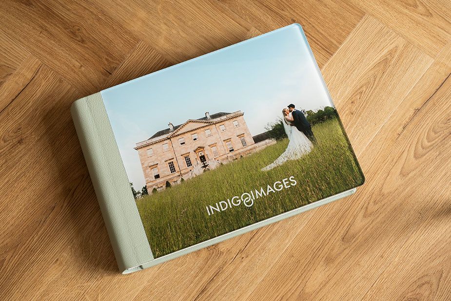 Professional wedding album with blue binding showing couple walking through summer meadow.