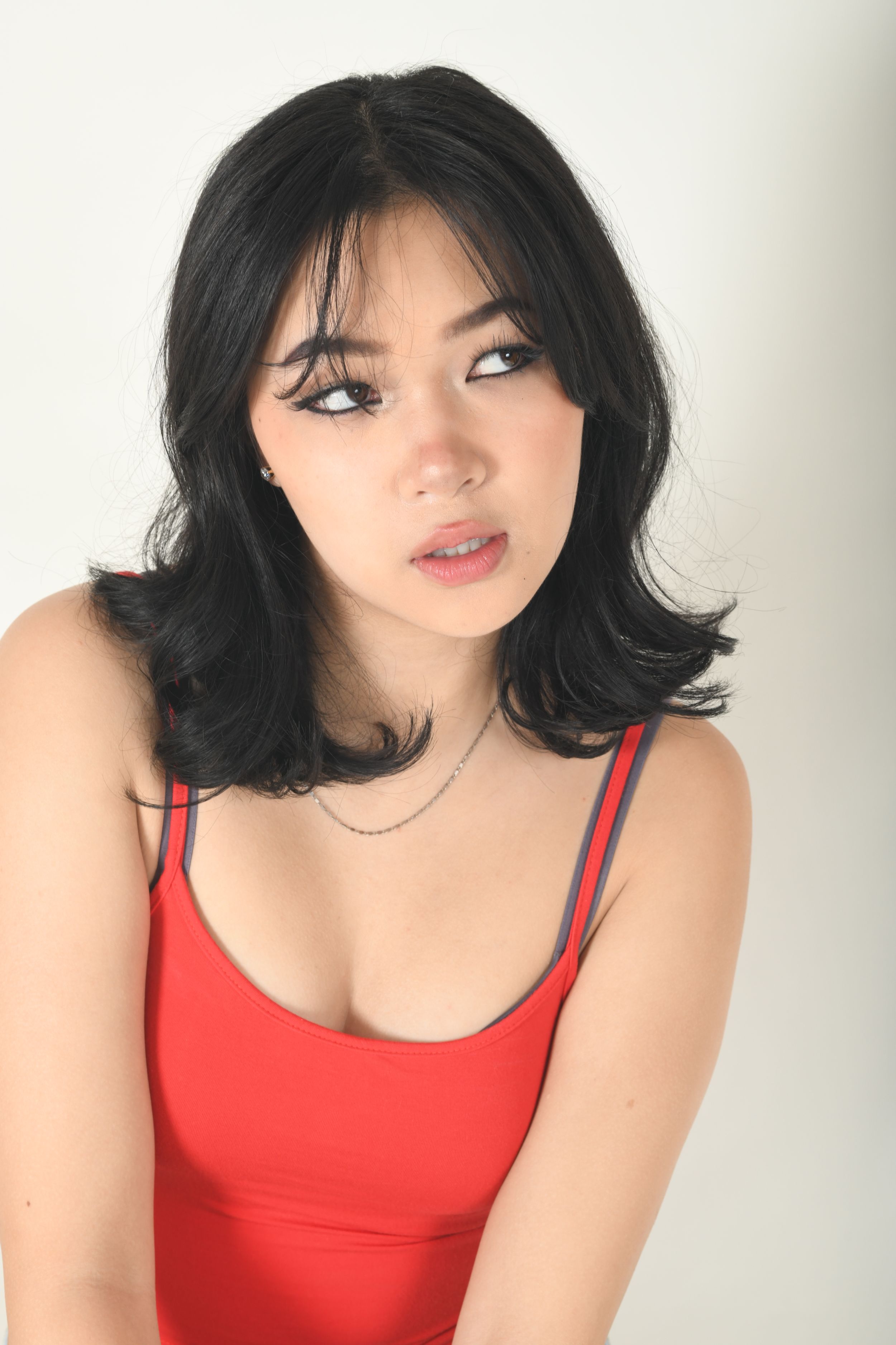Portrait in red tank top against white background with dramatic side glance.