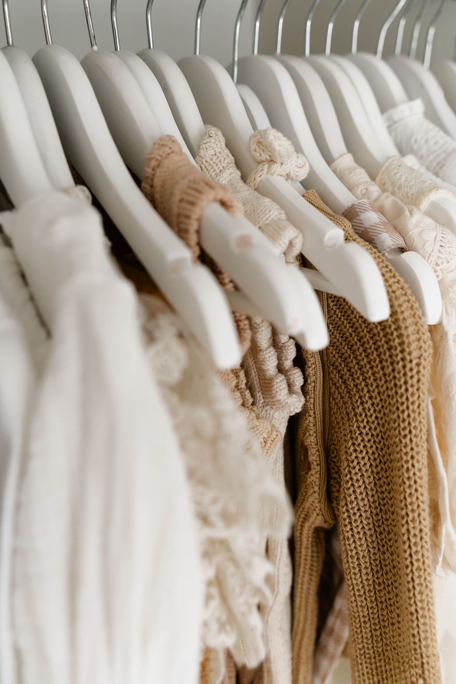 Neutral colored clothing hanging neatly on white hangers in a closet.