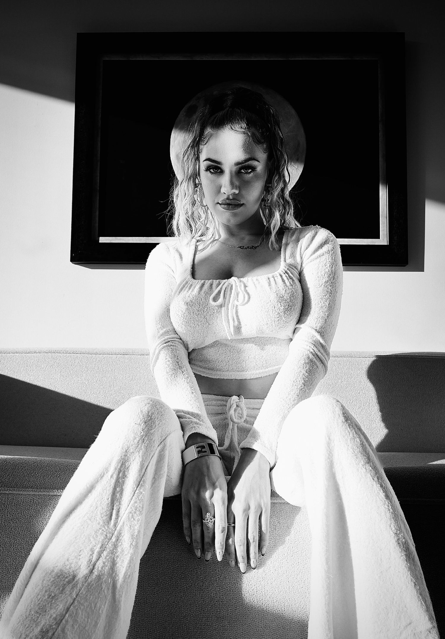Black and white portrait of a Model in all-white bohemian style outfit with a crop top and wide-leg pants sitting on a surface.