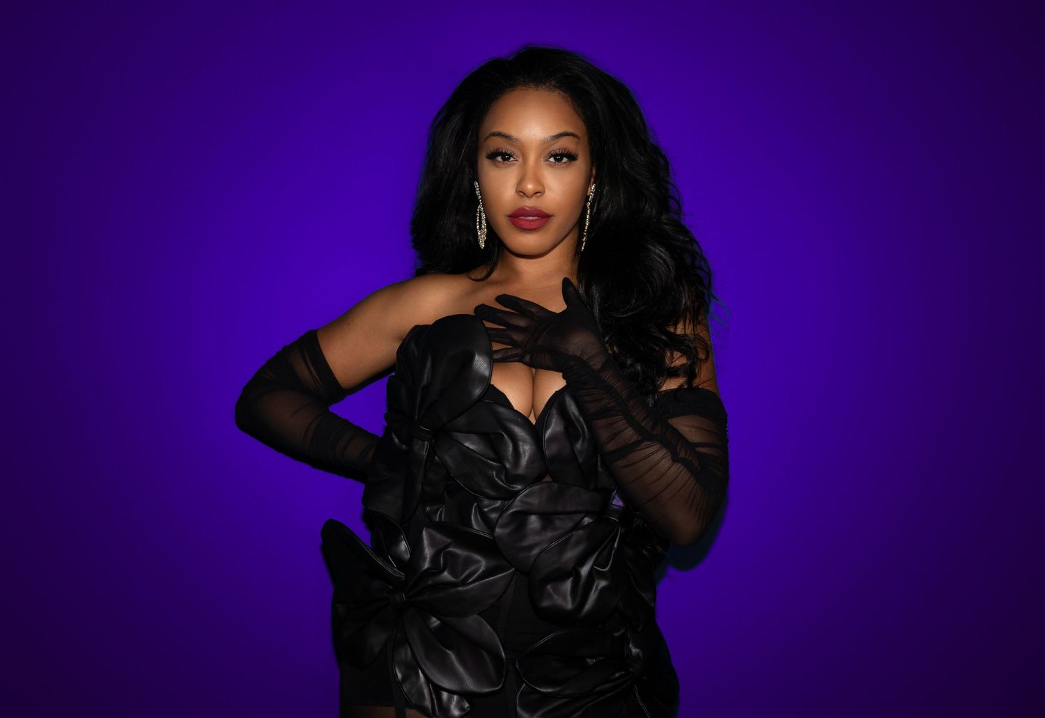 Dramatic portrait of person in black dress against purple background.