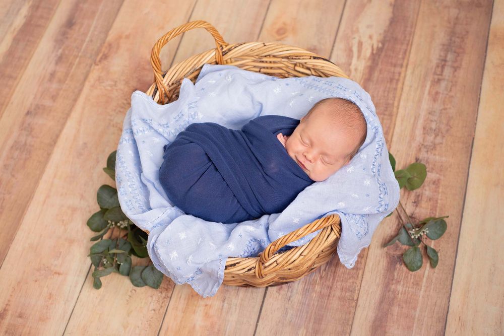 newborn baby boy in blue wrap sleeps in basket prop wrapped in navy blue blanket photographer Nicole Turk Photography*