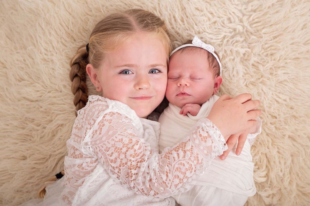 Big sister lovingly cuddles her newborn baby sister during a professional newborn photography session in studio near Cobourg, Ontario*