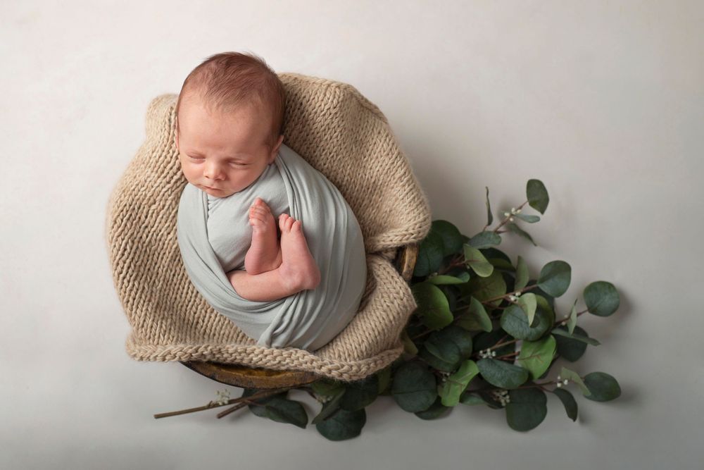 Northumberland newborn baby photographer of boy wrapped in sage green wrap posed in bowl prop with eucalyptus greens*