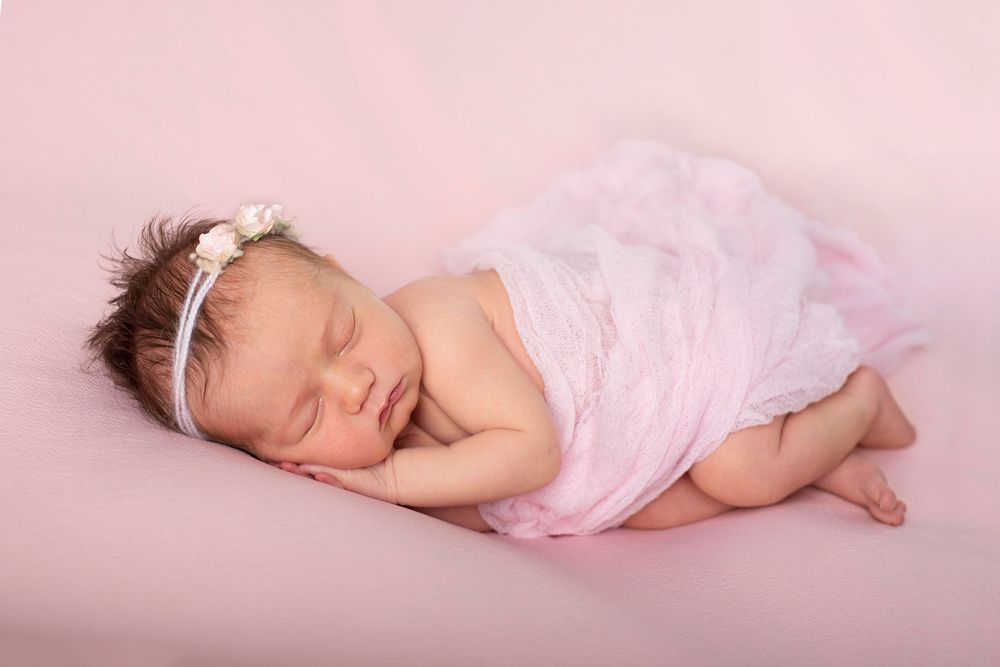 newborn in soft pink blanket with floral headband asleep on their side on a soft pink blanket. Baby photography Baltimore ON*