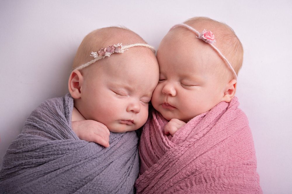 twin baby girls snuggle together wrapped in purple blankets with floral headbands for newborn session in Baltimore Ontario by Nicole Turk*