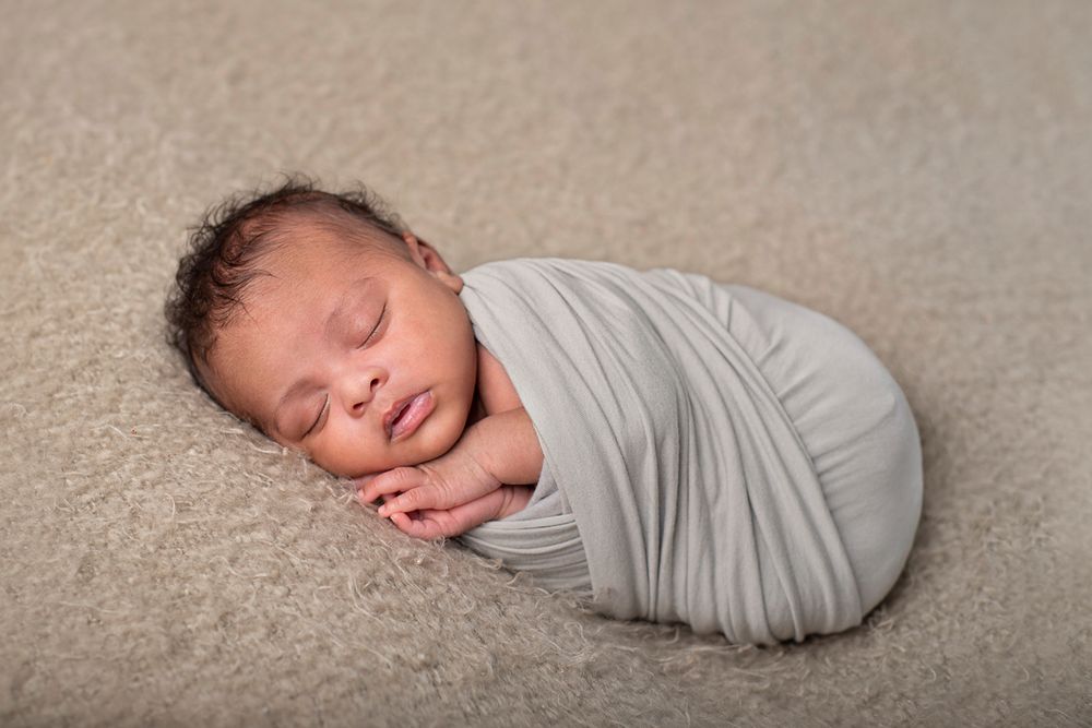Newborn baby boy fully wrapped posed on his side with his hand under his chin servicing Northumberland County*