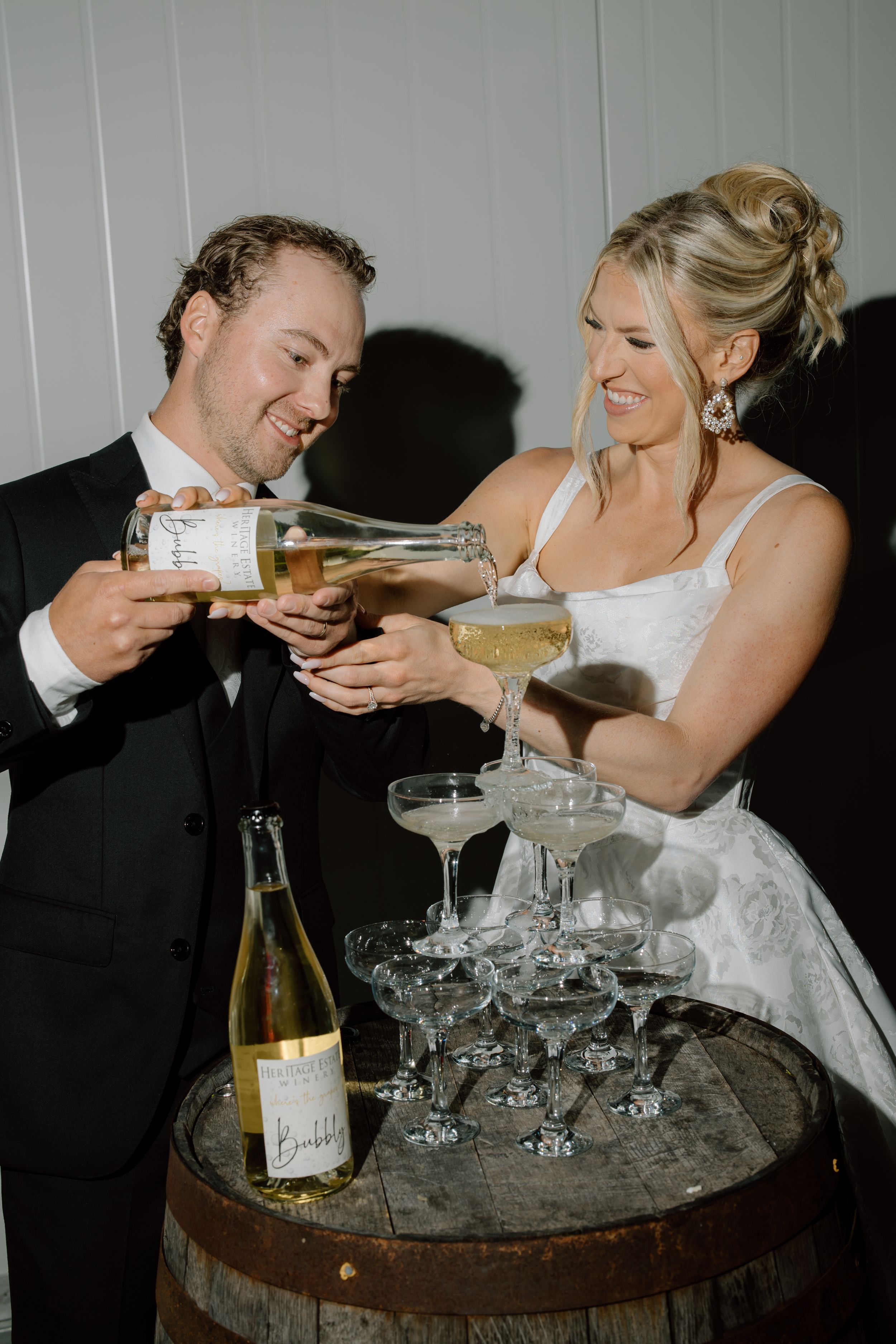 A sequence of wedding reception photos showing a couple sharing champagne with vintage coupe glasses on a rustic barrel table.