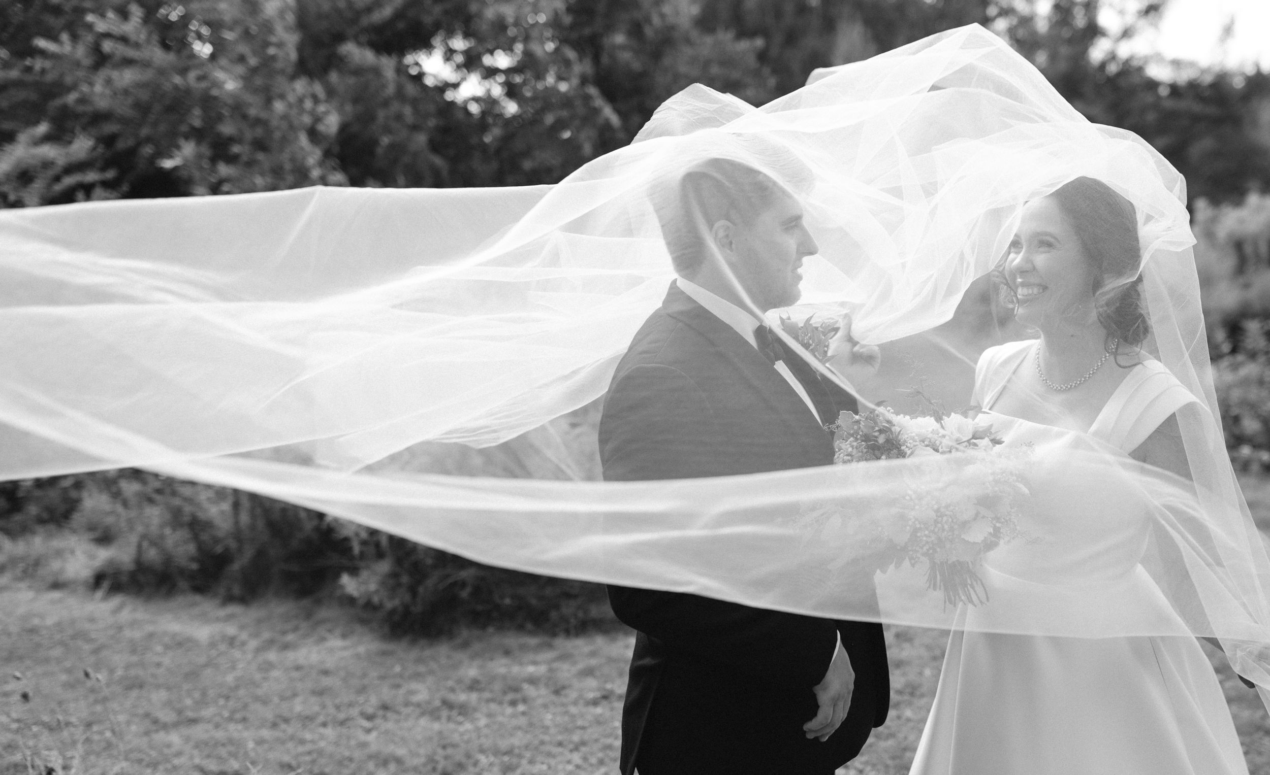 A flowing white veil billows gracefully in the wind during an outdoor wedding photoshoot.