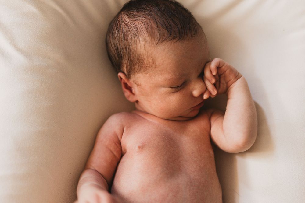 Peaceful newborn baby sleeping curled up on a soft cream blanket, showcasing delicate features and tiny hands.