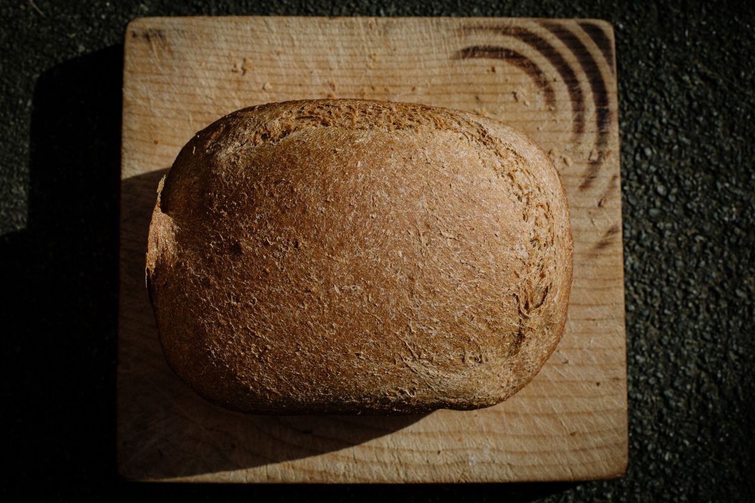 Round loaf of rustic bread on wooden cutting board with concentric circle patterns.