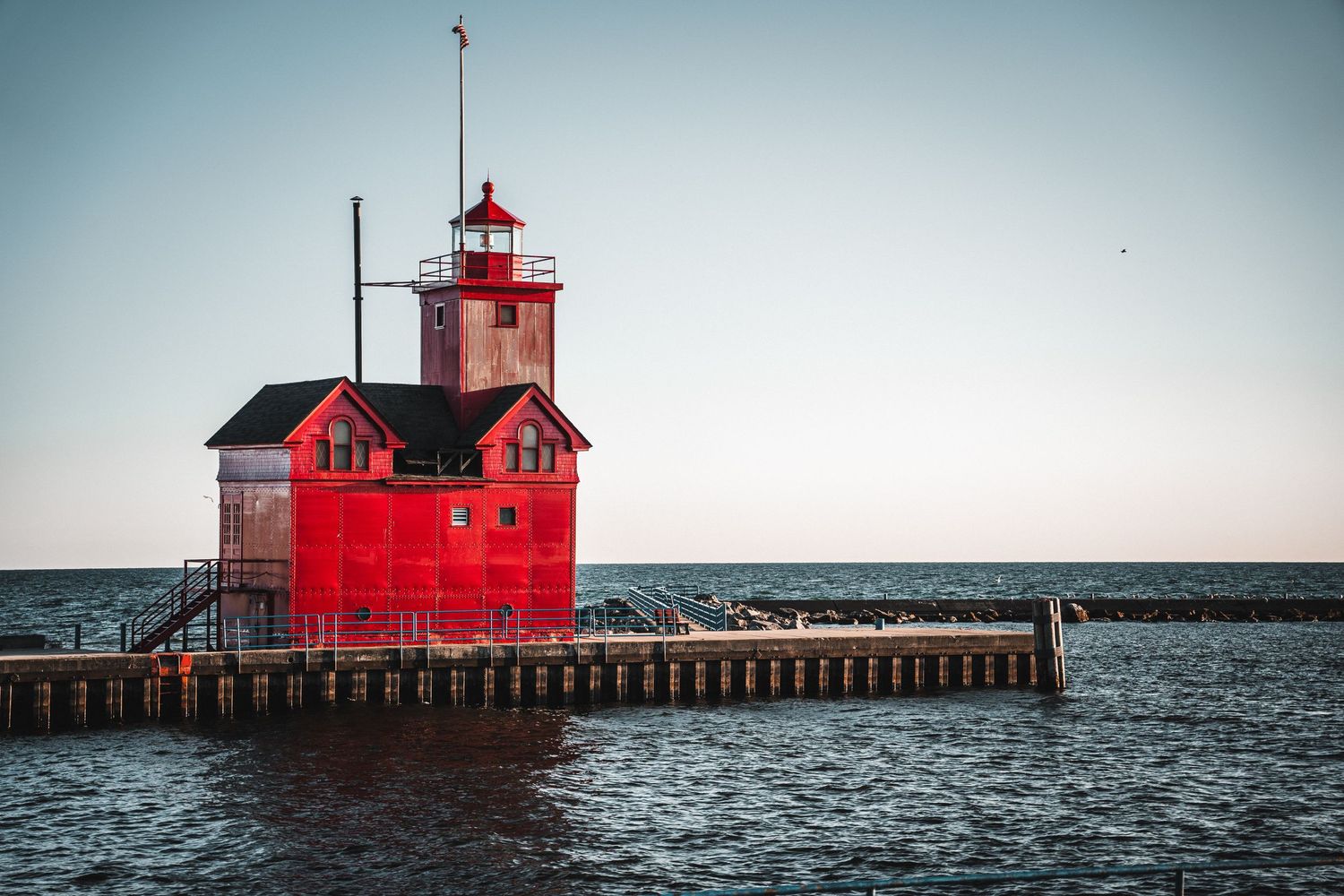 Iconic red Big Red Lighthouse on a pier surrounded by blue water under a clear sky.