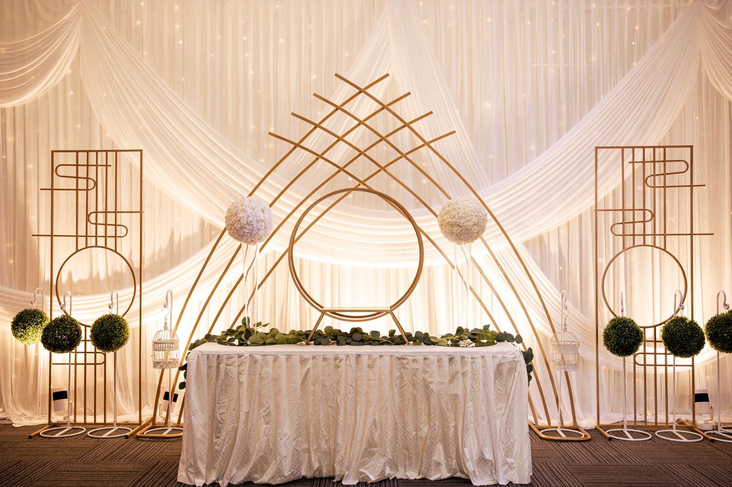 Modern wedding reception backdrop featuring geometric gold frames, circular white lanterns, and elegant white drapery.