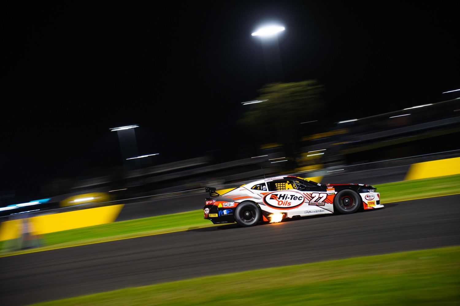 Race car speeds past on illuminated track during nighttime competition.